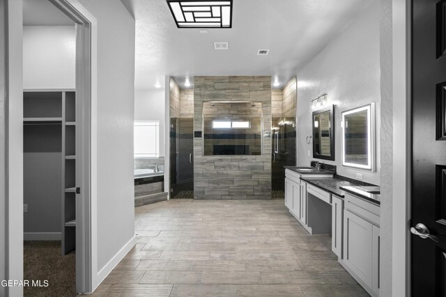 bathroom featuring a stall shower, a bath, double vanity, a spacious closet, and wood finished floors