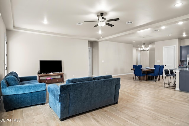 living room with a chandelier, a raised ceiling, a ceiling fan, light wood finished floors, and baseboards