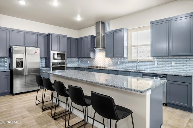 kitchen featuring stainless steel appliances, wall chimney range hood, a sink, a kitchen breakfast bar, and a center island