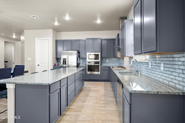 kitchen featuring appliances with stainless steel finishes, a sink, gray cabinetry, a kitchen island, and light stone countertops
