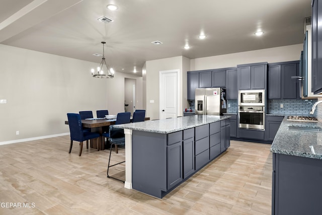 kitchen featuring appliances with stainless steel finishes, a kitchen island, light stone countertops, a chandelier, and a sink