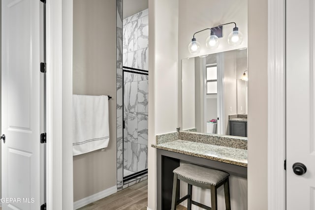 full bathroom featuring a marble finish shower, vanity, wood finished floors, and baseboards