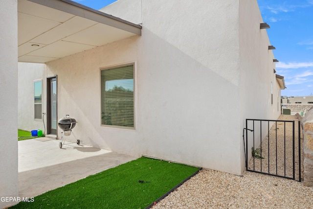view of property exterior with stucco siding, a patio area, and a gate