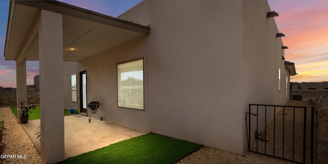 view of side of home with a patio area, stucco siding, fence, and a gate