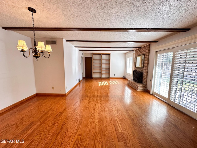3100 Hector Dr, El Paso, TX 79935 - unfurnished living room featuring a textured ceiling, beamed ceiling, a chandelier, a brick fireplace, and light wood-style floors