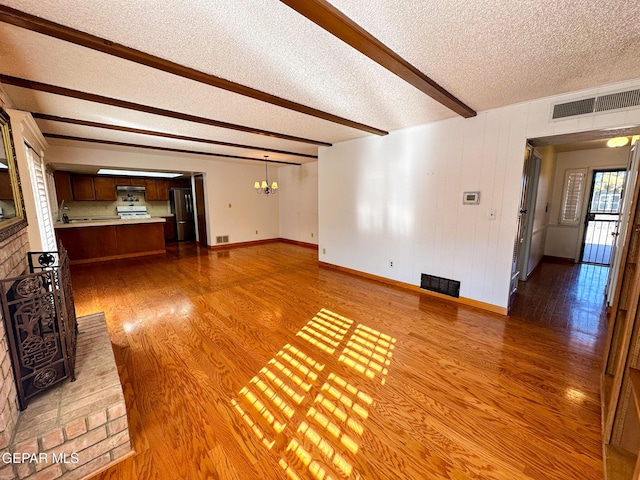 3100 Hector Dr, El Paso, TX 79935 - unfurnished living room with a textured ceiling, wood finished floors, baseboards, beam ceiling, and a chandelier