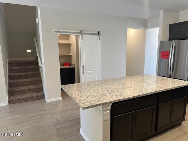 6112 Hidden Row Ave, El Paso, TX 79924 - kitchen featuring freestanding refrigerator, a barn door, light stone counters, and baseboards