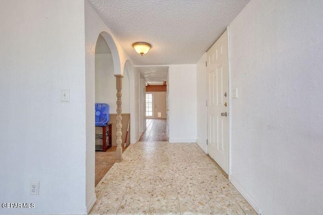 hallway featuring a textured ceiling, arched walkways, light floors, and baseboards
