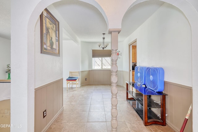 corridor featuring wainscoting, tile patterned floors, arched walkways, and wood walls