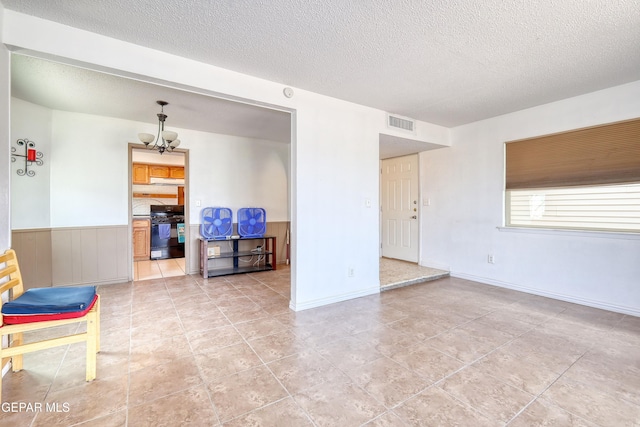 unfurnished living room with a textured ceiling, a chandelier, a wainscoted wall, and light tile patterned flooring