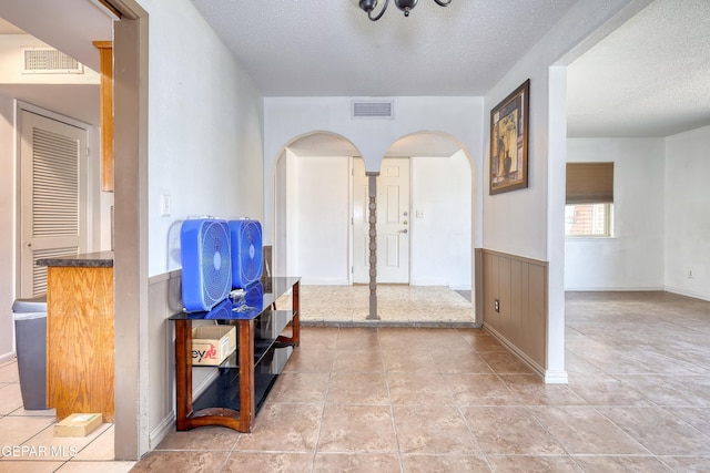 foyer with arched walkways, a textured ceiling, and a wainscoted wall