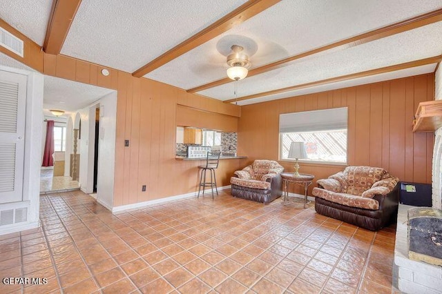 tiled living area featuring a textured ceiling, beam ceiling, ceiling fan, baseboards, and wooden walls