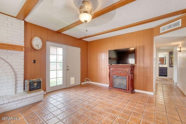unfurnished living room with a glass covered fireplace, ceiling fan, beamed ceiling, and a textured ceiling
