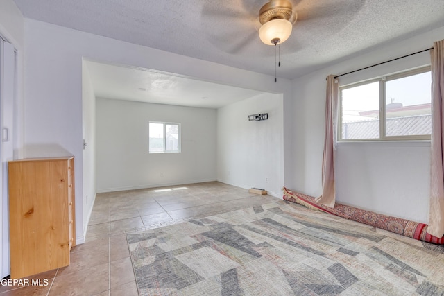 empty room featuring light tile patterned flooring, a ceiling fan, baseboards, and a textured ceiling