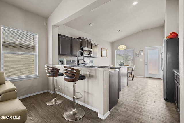 7421 Dewberry Dr, El Paso, TX 79911 - kitchen with vaulted ceiling, stainless steel appliances, light wood finished floors, a kitchen breakfast bar, and dark brown cabinets