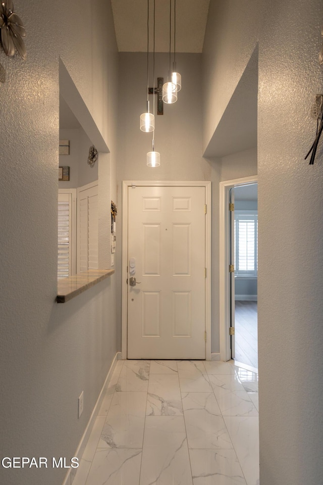 foyer entrance with baseboards, a high ceiling, light marble finish flooring, and a textured wall