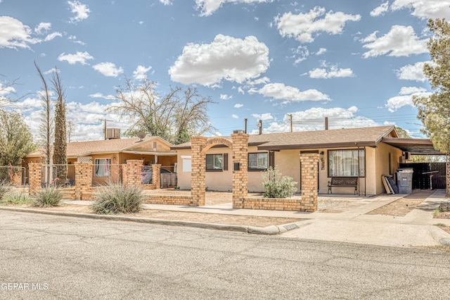 ranch-style house with a fenced front yard, stucco siding, driveway, an attached carport, and a gate