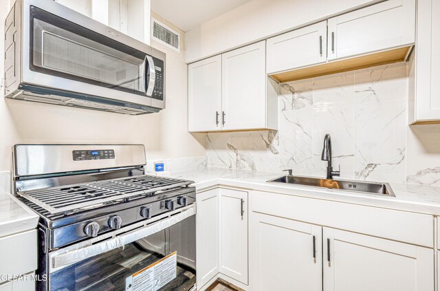 kitchen with appliances with stainless steel finishes, a sink, white cabinets, and tasteful backsplash