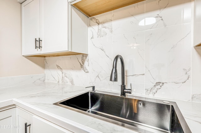 kitchen with a sink, white cabinets, tasteful backsplash, and light stone counters