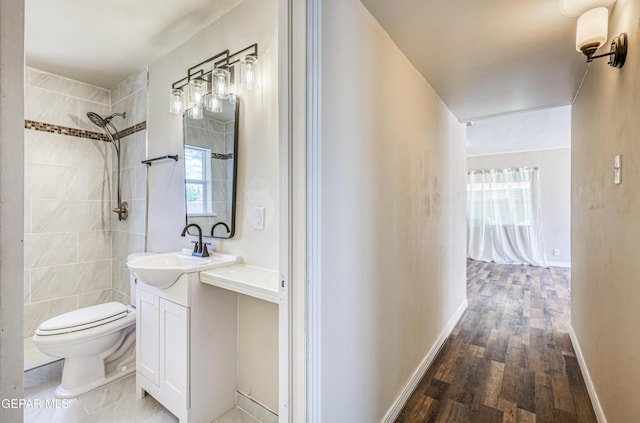 bathroom featuring wood finished floors, toilet, vanity, baseboards, and a tile shower