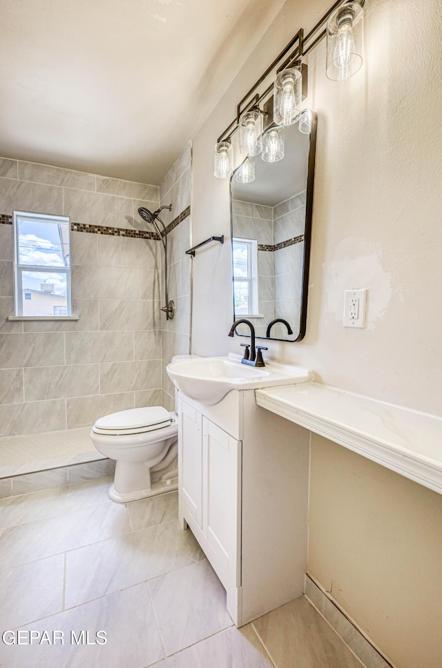 bathroom featuring a tile shower, toilet, vanity, and tile patterned flooring