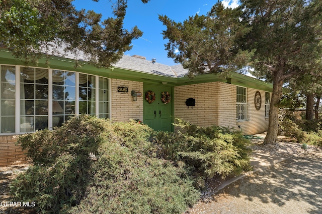 view of front of property featuring brick siding and roof with shingles