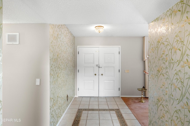 entryway featuring wallpapered walls, baseboards, a textured ceiling, and tile patterned floors