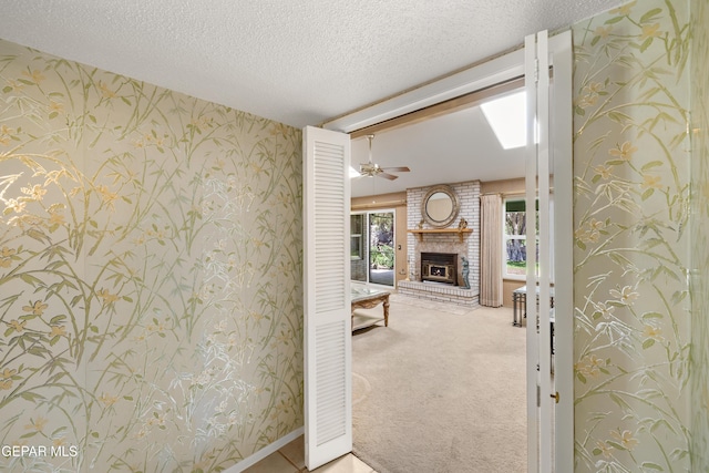 unfurnished living room featuring wallpapered walls, a fireplace, a textured ceiling, carpet floors, and ceiling fan