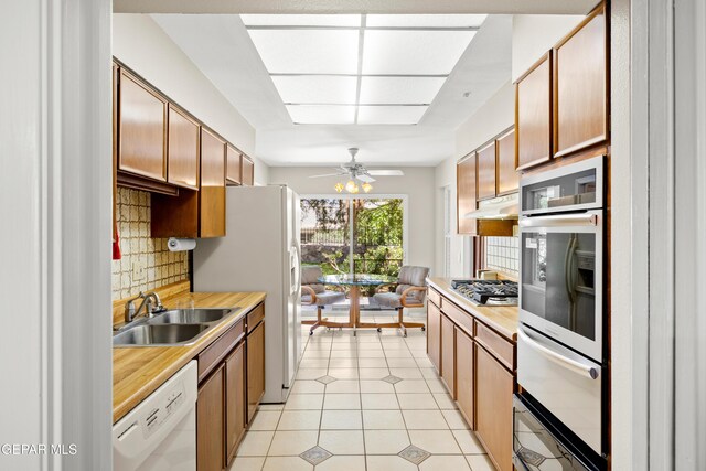 kitchen featuring white appliances, a sink, decorative backsplash, light countertops, and under cabinet range hood
