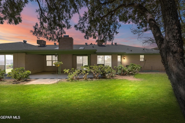 back of property at dusk with a patio area, a chimney, a yard, and brick siding