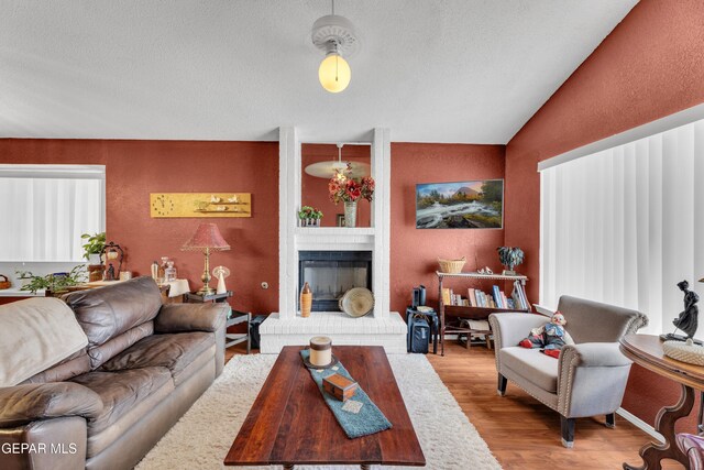 12273 El Greco Cir, El Paso, TX 79936 - living room featuring a brick fireplace, wood finished floors, vaulted ceiling, a textured ceiling, and a textured wall