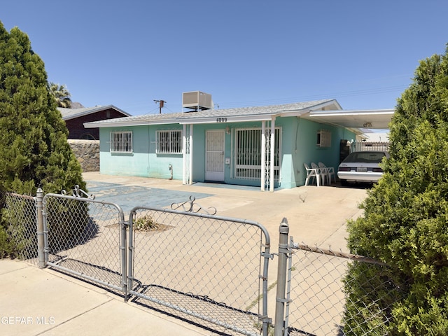 view of front of house featuring a gate, stucco siding, a carport, and central AC
