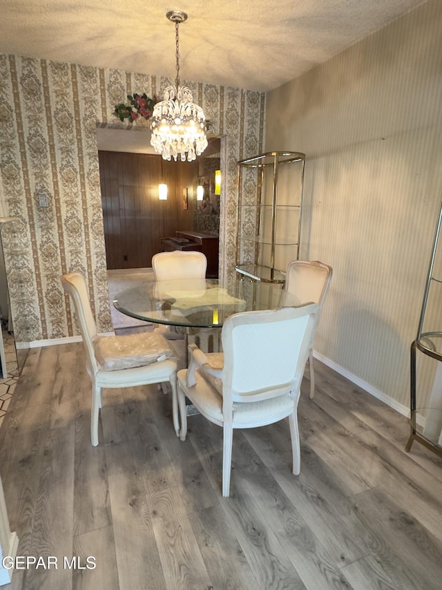 dining space with wallpapered walls, wood finished floors, a chandelier, and baseboards