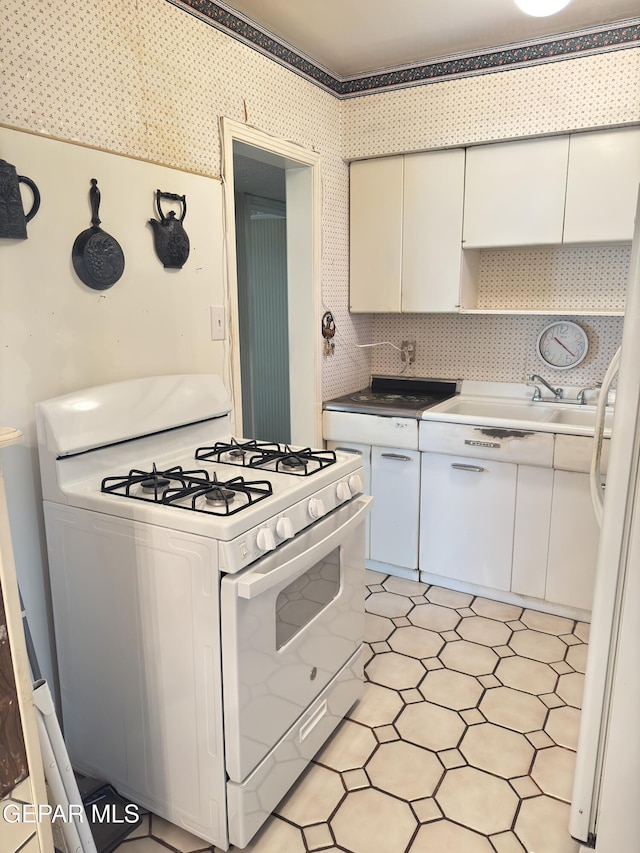 kitchen featuring white appliances, a sink, backsplash, and white cabinetry