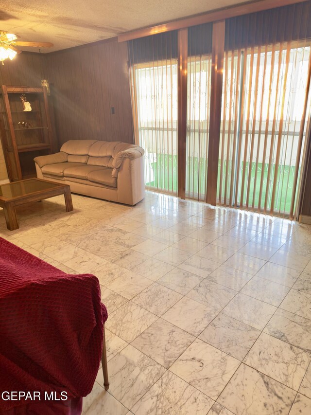 living room featuring marble look tiles, wooden walls, and ceiling fan