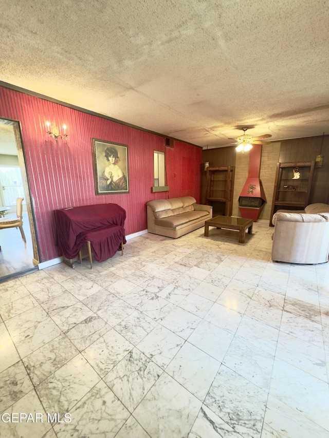living room featuring a ceiling fan, marble look tiles, wooden walls, a textured ceiling, and baseboards