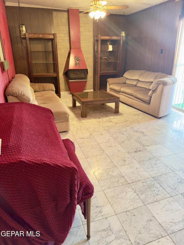 living room with wooden walls, marble finish floors, ceiling fan, and a wood stove