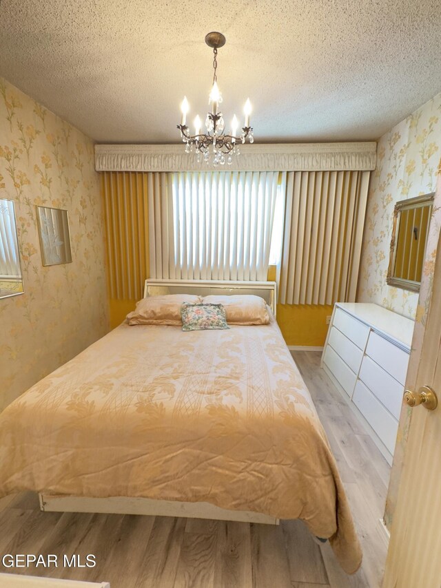 bedroom featuring wallpapered walls, wood finished floors, a chandelier, and a textured ceiling