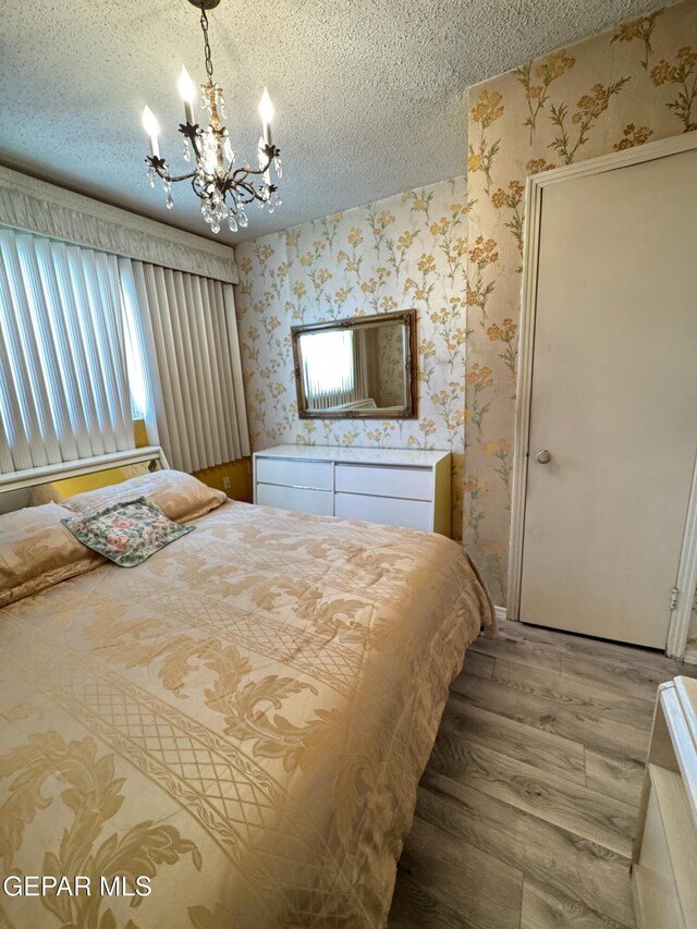bedroom featuring wallpapered walls, light wood-type flooring, a chandelier, and a textured ceiling