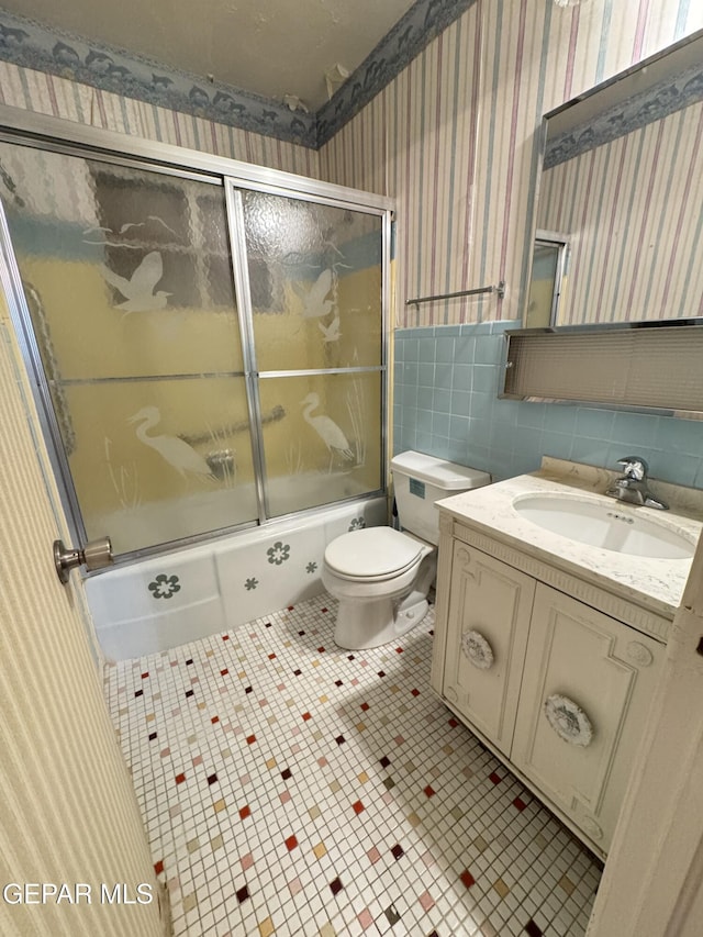 full bath featuring wallpapered walls, shower / bath combination with glass door, vanity, tile patterned floors, and a wainscoted wall