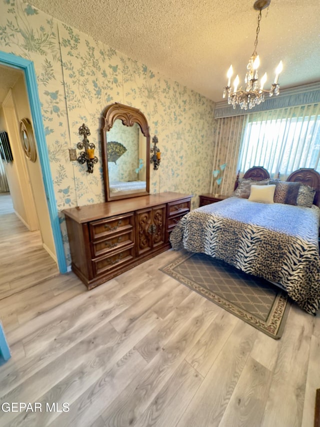 bedroom featuring wallpapered walls, a chandelier, a textured ceiling, wood finished floors, and baseboards
