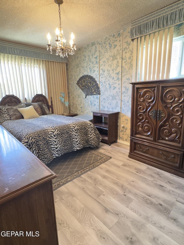 bedroom with wallpapered walls, a chandelier, wood finished floors, a textured ceiling, and baseboards
