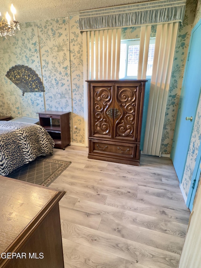bedroom featuring wallpapered walls, light wood-style floors, and a textured ceiling