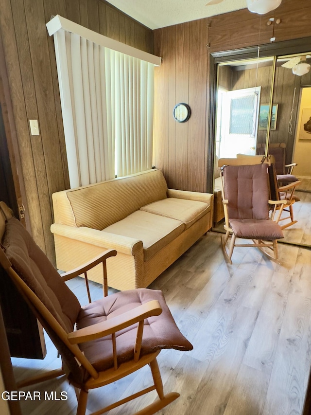 living area featuring wooden walls, wood finished floors, and ceiling fan
