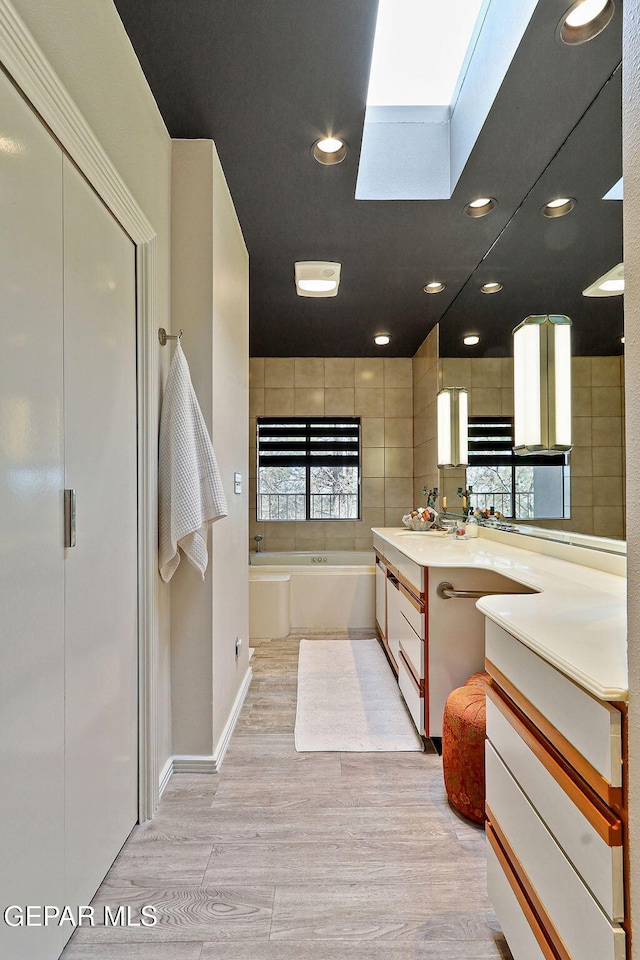 1114 Los Jardines Cir, El Paso, TX 79912 - bathroom featuring wood finished floors, a garden tub, a skylight, vanity, and baseboards
