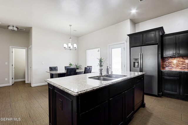 12748 Barstow Ave, El Paso, TX 79928 - kitchen with stainless steel fridge, dark cabinetry, an island with sink, and a chandelier