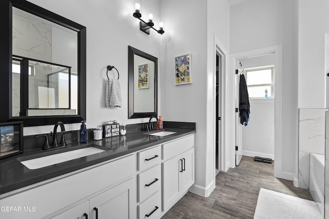 full bath with a bath, a shower with shower door, baseboards, double vanity, and wood finished floors
