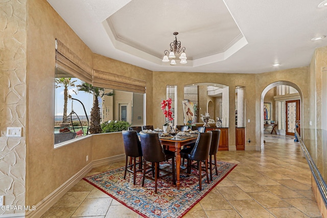 6664 Tuscany Ridge Dr, El Paso, TX 79912 - dining area with arched walkways, a chandelier, baseboards, a tray ceiling, and light stone finish flooring