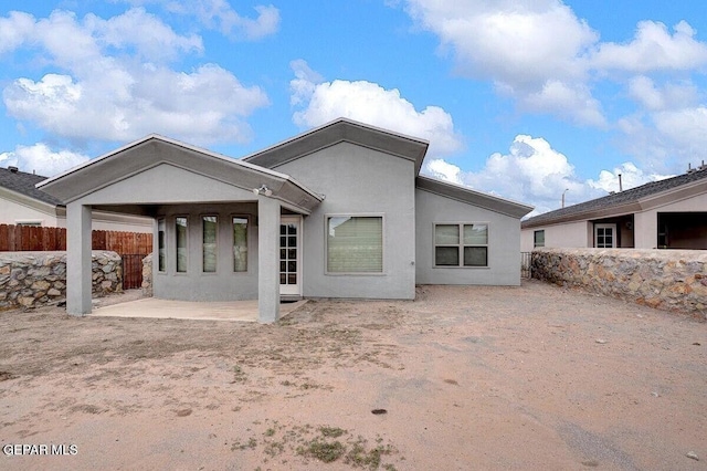 rear view of property featuring stucco siding, fence, and a patio area