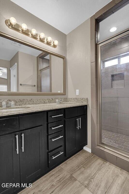 full bathroom with double vanity, a stall shower, and wood finished floors